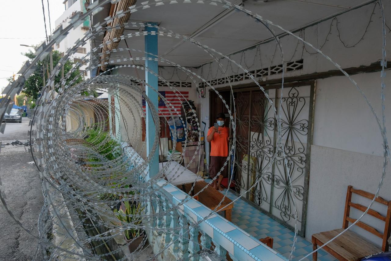 A man snaps a picture of the barbed wire fence surrounding his home in Kampung Segambut Dalam, which has placed under enhanced movement control order. Photo: Bernama