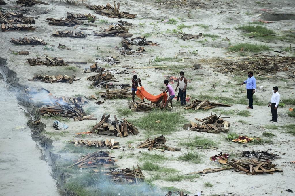 Municipal corporation workers prepare to cremate a body buried in a shallow grave on the banks of the Ganges river during the Covid-19 pandemic as they cremate other bodies also buried there to prevent them from floating downstream as water levels increase near Phaphamau Ghat, in Allahabad, June 25. Photo: AFP