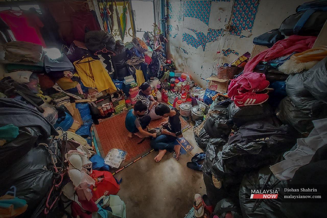 Rubi and her two children in their rented room in Lorong Haji Taib, Chow Kit Road in Kuala Lumpur. The family's belongings tower in stacks around the walls, leaving them only a small space in the middle.