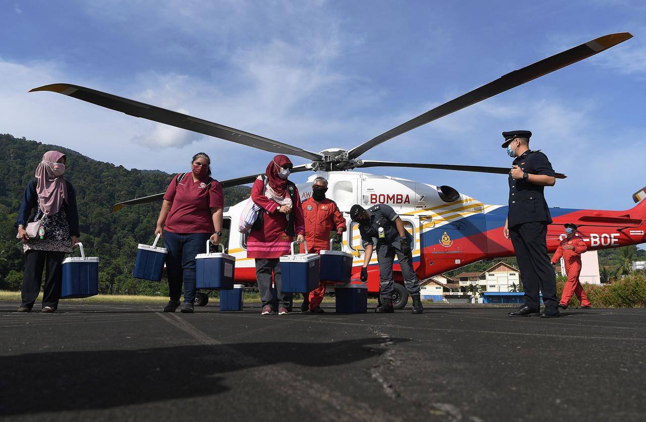 Medical workers carrying supplies of Covid-19 vaccine disembark from a helicopter from the fire and rescue department at Pulau Tioman. Photo: Bernama