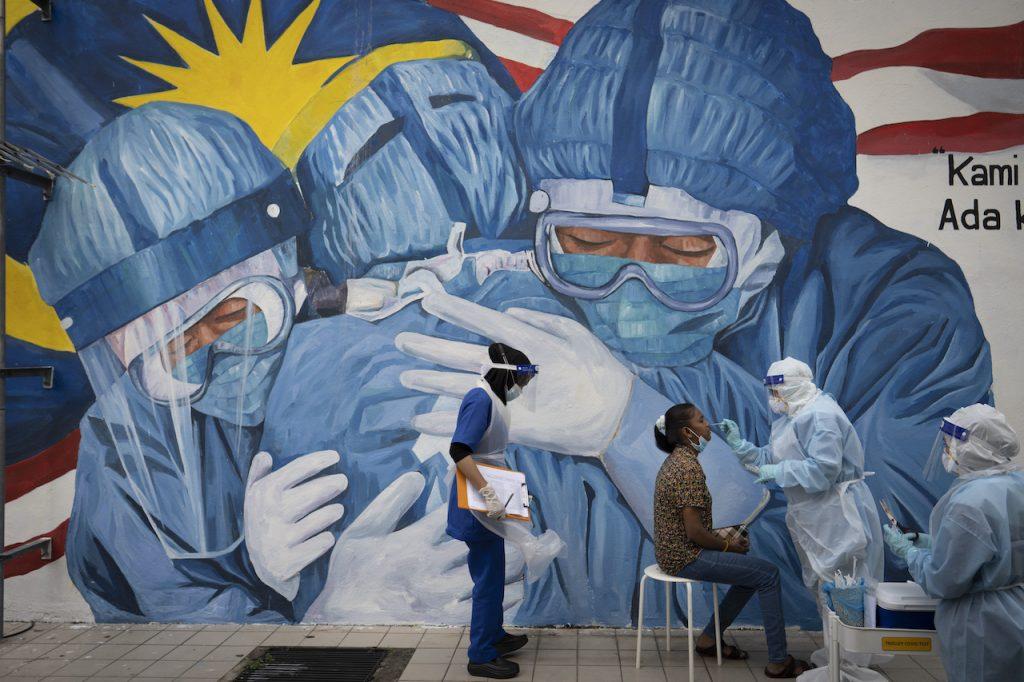A doctor collects a sample for testing at a Covid-19 screening facility near a mural depicting medical frontliners in Shah Alam, Selangor, on Dec 12, 2020. A group of contract doctors say they are still waiting to learn whether they have been absorbed into permanent positions in the government. Photo: AP