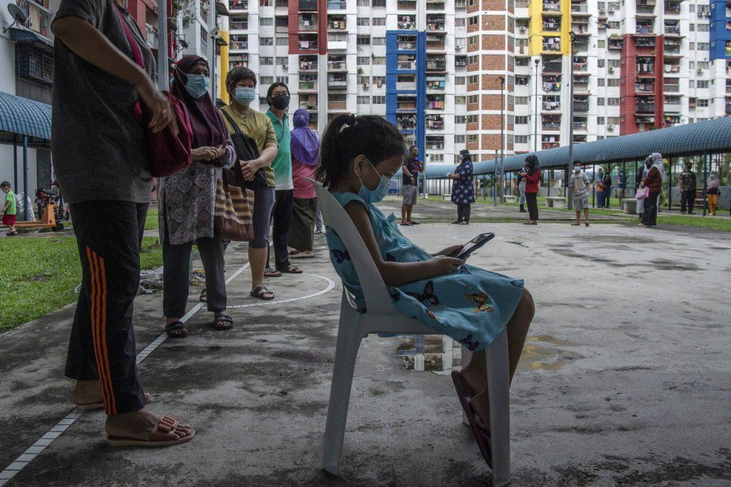 A girl plays with a phone while waiting in line to be screened for Covid-19 at a public housing area in Kuala Lumpur. Unicef says the pandemic and measures such as lockdowns have had negative effects on the mental health of many, including the youth. Photo: Bernama