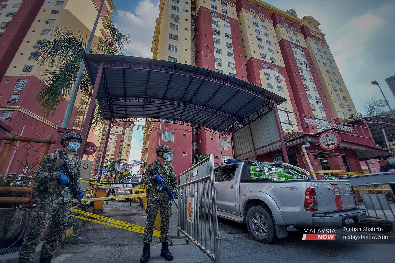 Military personnel monitor the main entrance of the Mentari Court flats in Petaling Jaya, Selangor, which have been placed under enhanced movement control order ahead of many other areas where tighter restrictions will begin tomorrow.