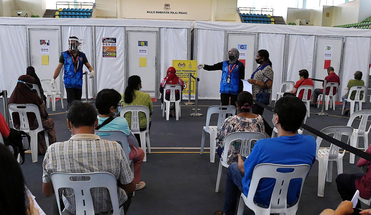 Volunteers direct people at the Kompleks Sukan Balik Pulau vaccination centre. Photo: Bernama