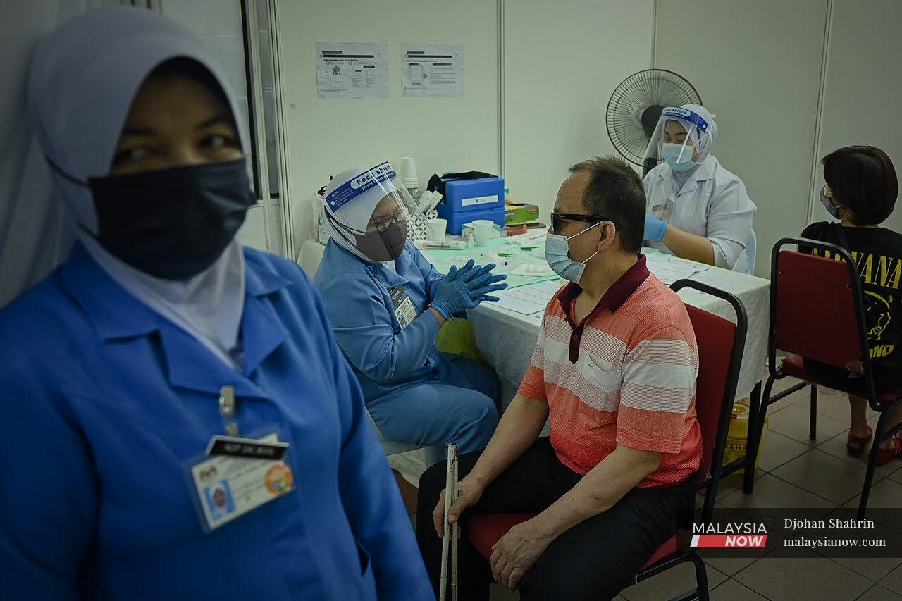 Seorang orang kelainan upaya cacat penglihatan berkata sesuatu kepada pegawai kesihatan sebelum menerima vaksin dos kedua Pfizer BioNTech di Persatuan Orang Buta Malaysia (MAB), Jalan Tebing, Brickfield.