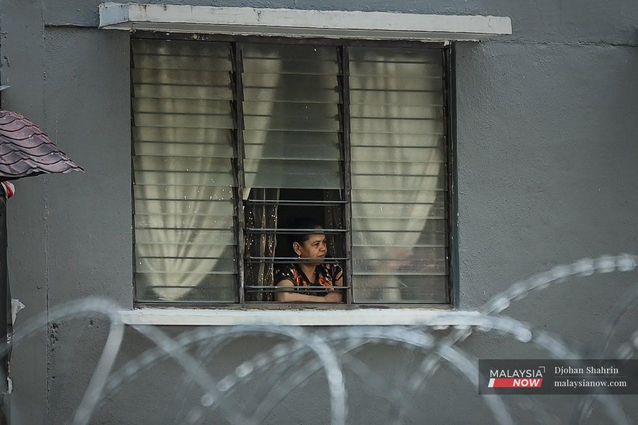A resident at Taman Bukit Angkasa, Kuala Lumpur, looks out her window at the barbed wire surrounding the area which has been placed under enhanced movement control order until July 14.