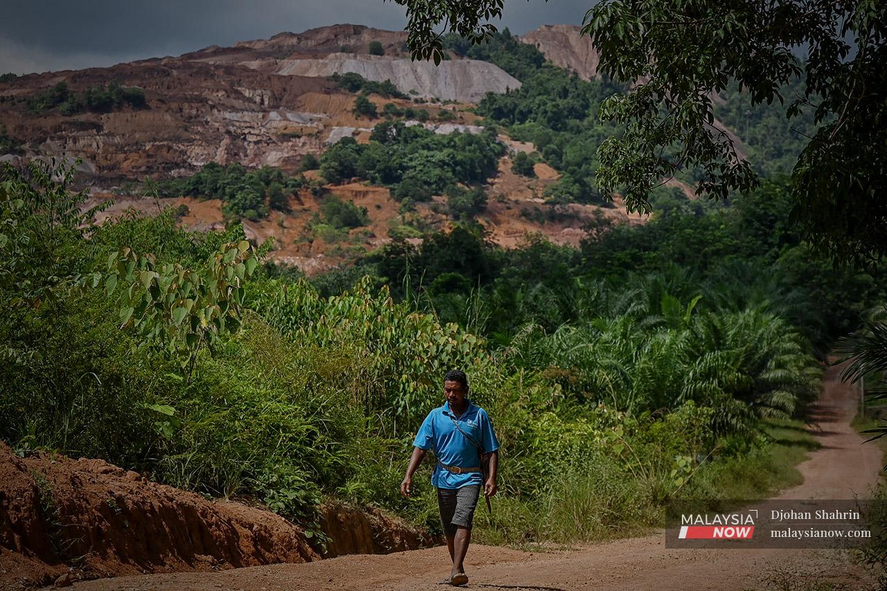 An Orang Asli man walks up a path near a hill laid bare by logging and mining activities near Tasik Chini in Pahang.