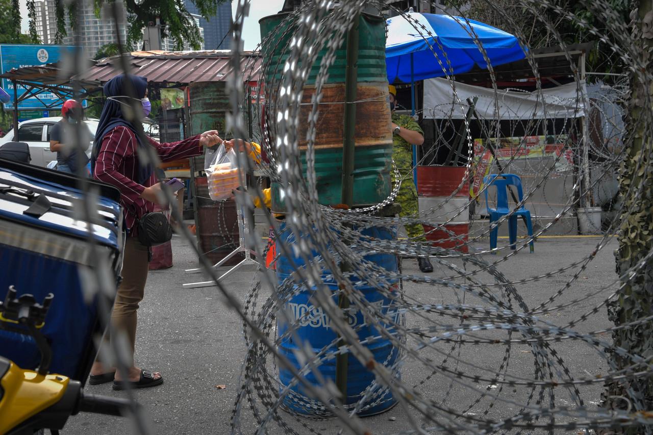 A woman passes a bag of food through the barbed wire barrier put up around the Taman Bukit Angkasa area which has been placed under enhanced movement control order until July 14. Photo: Bernama