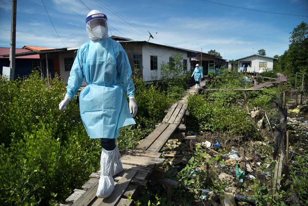 Health workers in personal protective equipment follow a walkway made of wooden planks as they go from house to house at the refugee community settlement scheme in Kampung Muslim, Labuan, to conduct targeted screening for Covid-19. Photo: Bernama