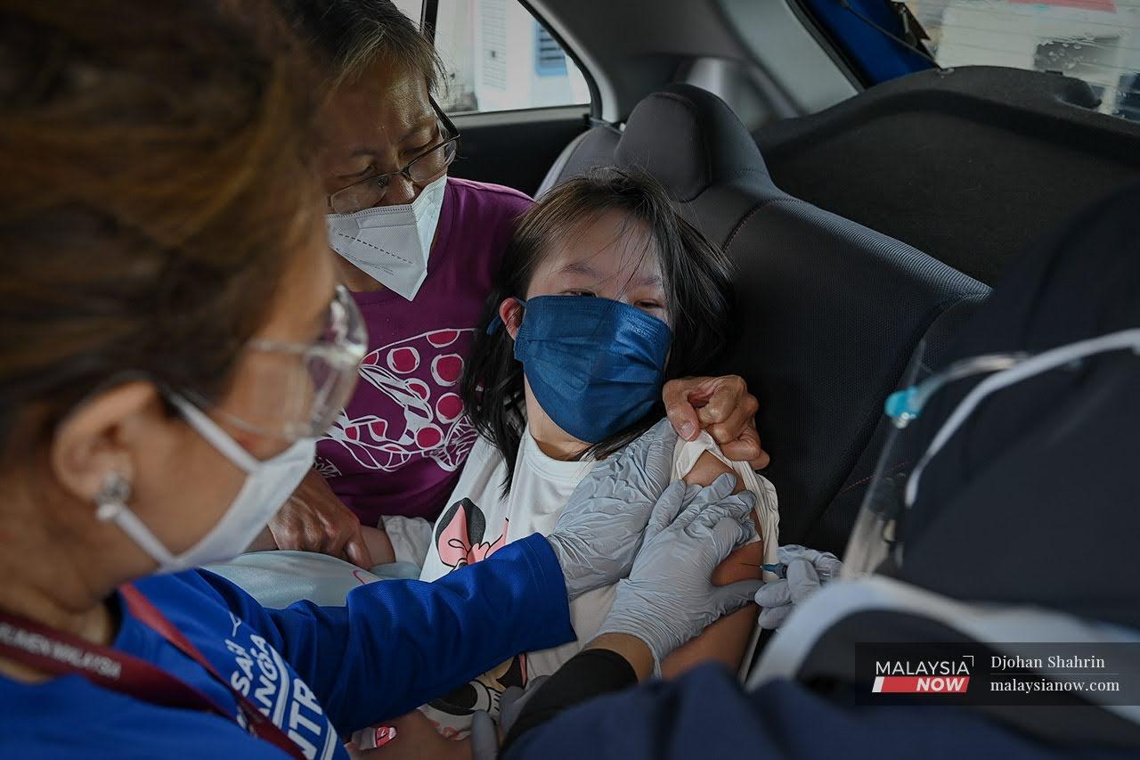 A health worker administers a shot of Sinovac Covid-19 vaccine to a girl with special needs at a drive-thru vaccination centre at Menara Same Darby Plantation at Subang in Selangor.