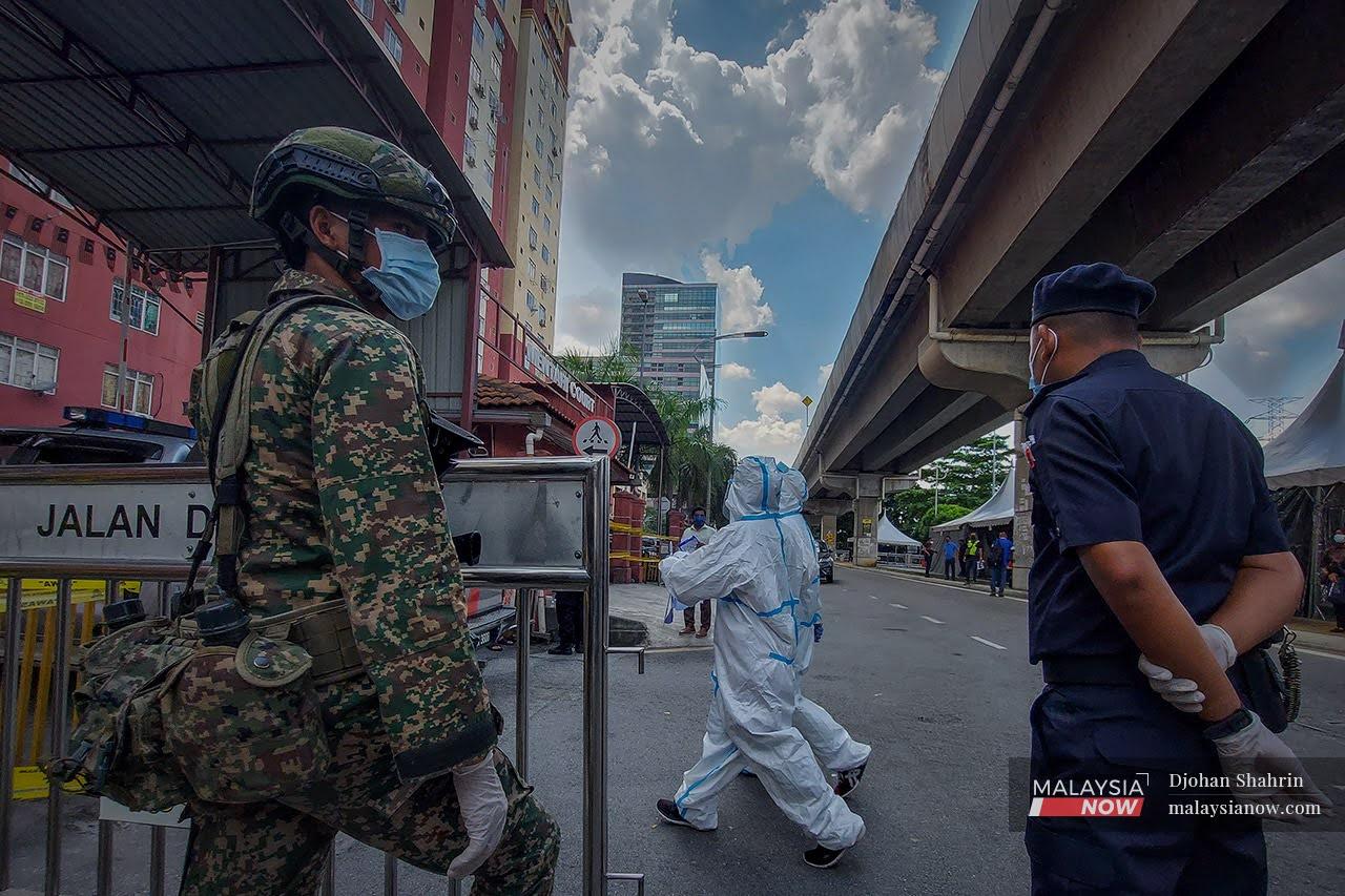 Personnel from the police and armed forces monitor the entrance of the Mentari Court flats in Petaling Jaya, Selangor, while health workers in personal protective equipment cross a street in front of them on the first day of the enhanced movement control order declared in the area earlier this month.
