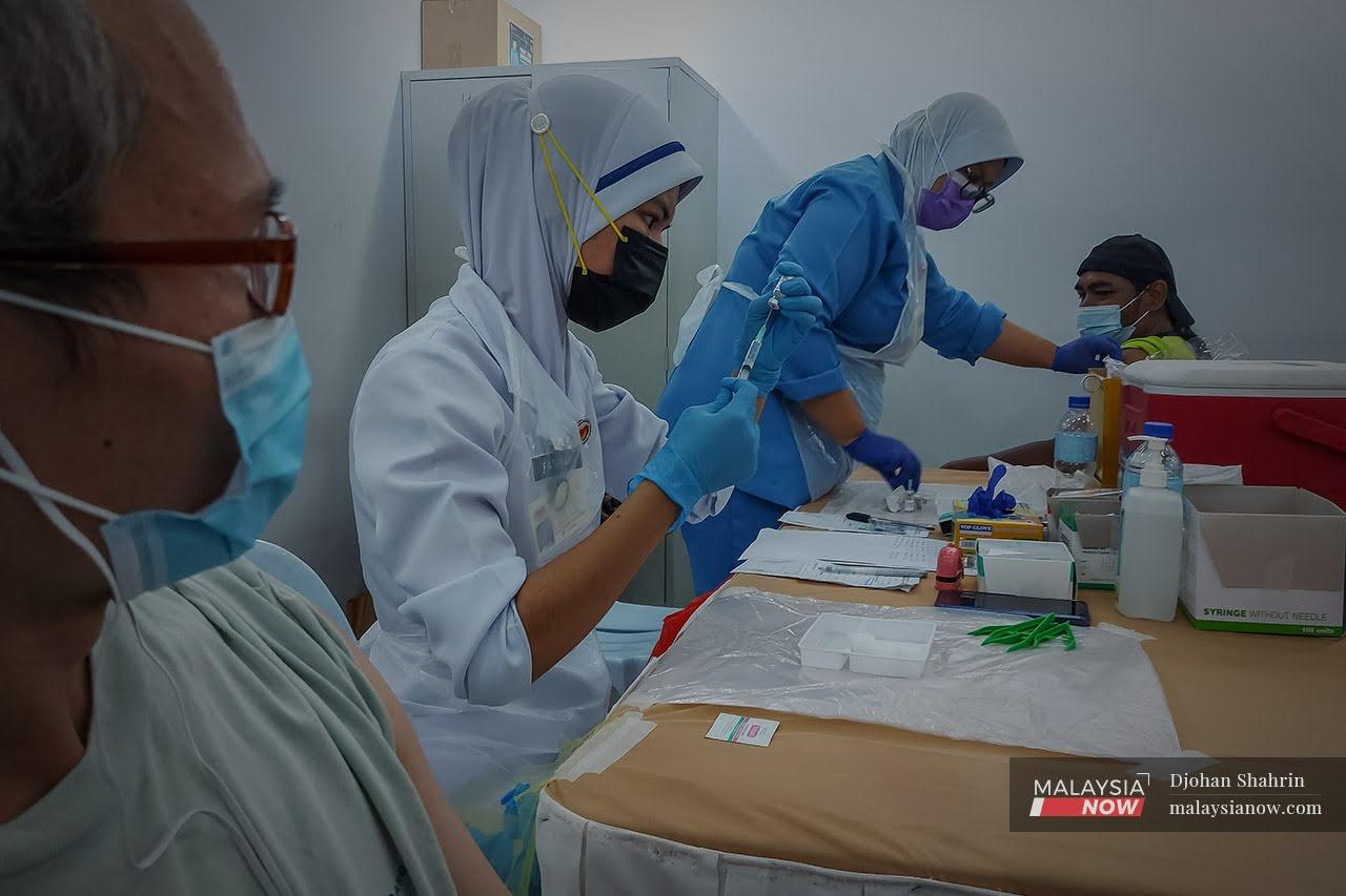 Petugas kesihatan dari Pusat Kesihatan Tangling membuat persediaan vaksin sebelum memberikan suntikan dos kedua kepada penghuni Pusat Transit Gelendangan Kuala Lumpur di Anjung Kelana, Taman Desa, Kuala Lumpur.