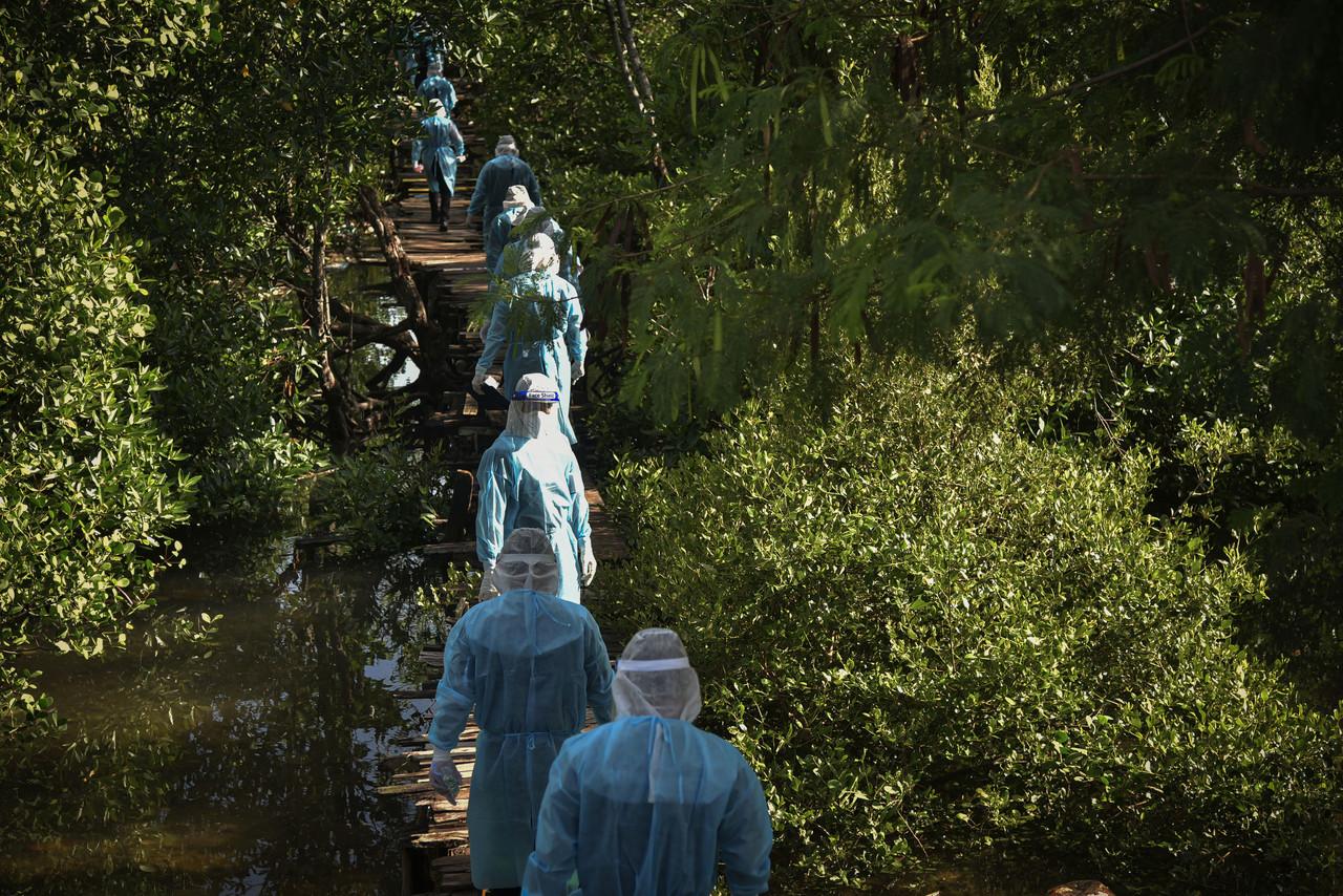 Police wearing personal protective equipment accompany medical workers conducting Covid-19 screening at a refugee community settlement scheme in Kampung Muslim, Labuan. Photo: Bernama