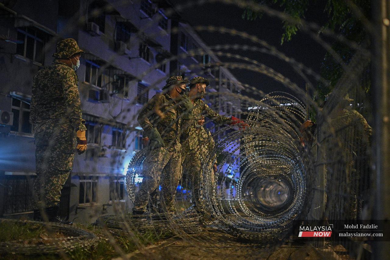 Armed forces personnel unroll the coils of barbed wire that have become synonymous across the country with the implementation of enhanced movement control order or EMCO.