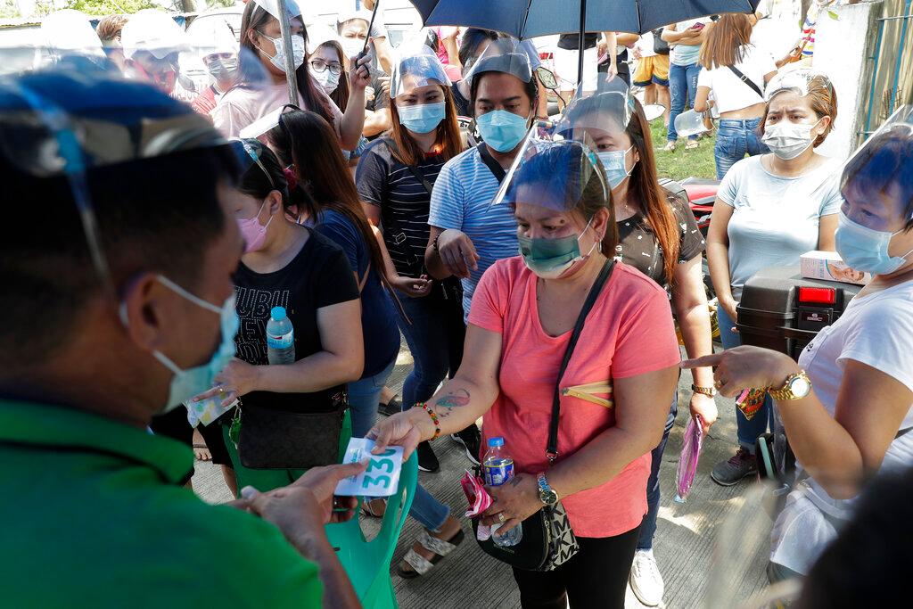 A woman is handed a number as she waits for her turn to be vaccinated with others outside a temporary vaccination centre at the Navotas Fish Port, Philippines, June 7. Photo: AP