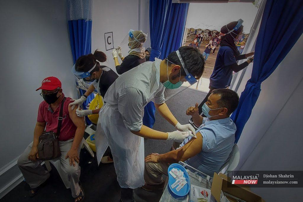 Health workers administer doses of the Sinovac vaccine to residents of the Pantai Ria flats at a mobile vaccination centre in Pantai Dalam.