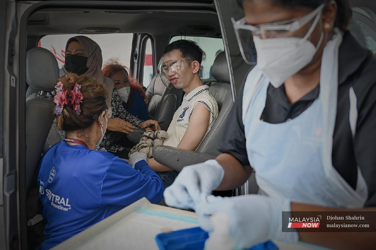 Petugas kesihatan Pusat Perubatan Ara Damansara membuat persiapan sebelum memberi suntikan vaksin Sinovac kepada seorang orang kelainan upaya (oku) secara pandu lalu di Pusat Pemberian OKU di Menara Sime Darby Plantation, Subang.