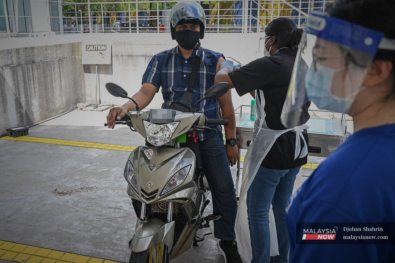 Petugas kesihatan Pusat Perubatan Ara Damansara memberi suntikan vaksin Sinovac kepada penunggang motosikal secara pandu lalu di Pusat Pemberian Vaksin Orang Kelainan Upaya (OKU) di Menara Sime Darby Plantation, Subang.