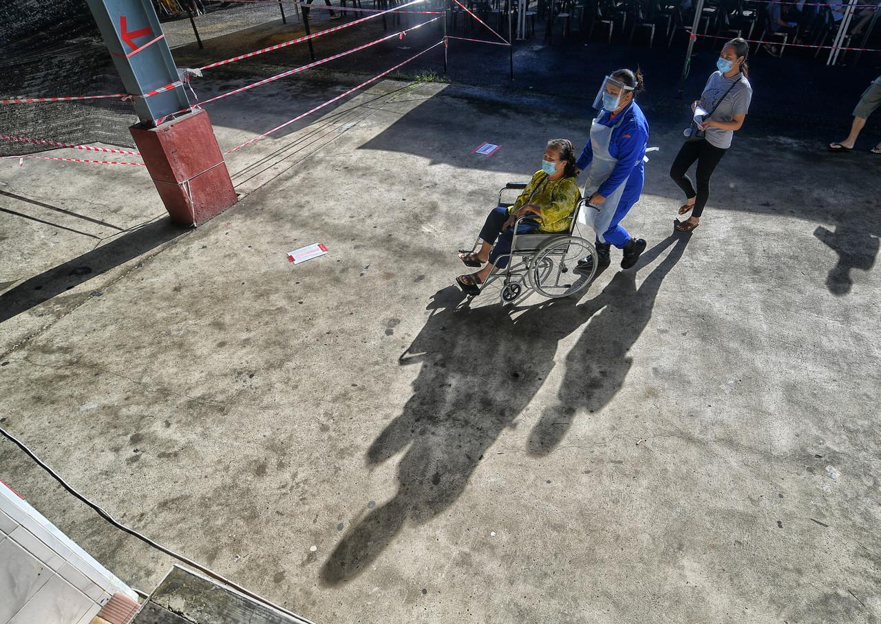 A member of the Sarawak Civil Defence Force pushes a senior citizen in a wheelchair to receive a jab of Covid-19 vaccine at the vaccination centre in Siburan. Photo: Bernama
