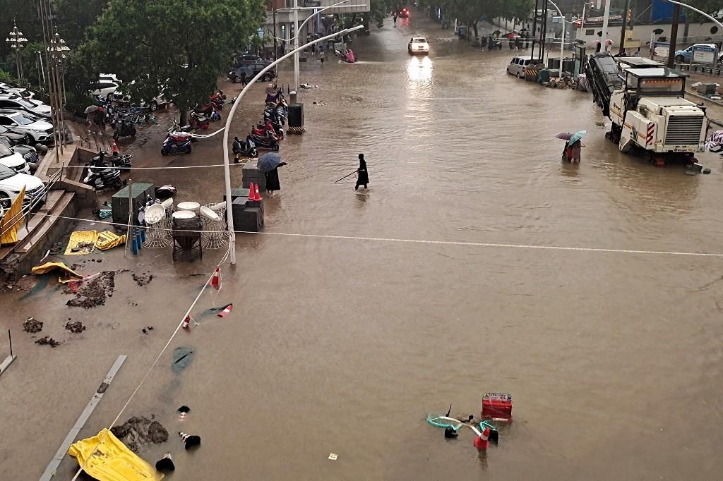This photo taken on July 20 shows people wading through flood waters along a street following heavy rains in Zhengzhou in China's central Henan province. Photo: AFP