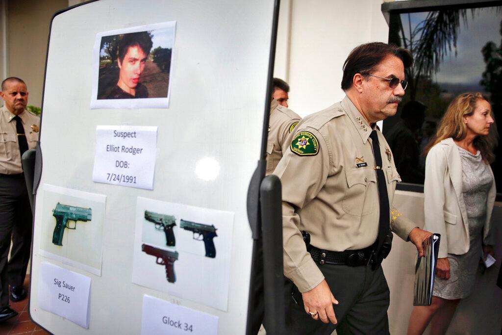A Santa Barbara law enforcement officer (right) walks past a board displaying photos of suspected gunman Elliot Rodger and the weapons he used in a mass shooting in Isla Vista, California in this May 24, 2014 file photo. Photo: AP