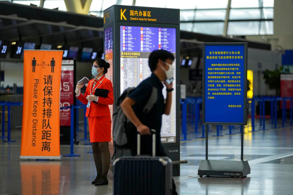 A passenger wearing a face mask to help curb the spread of the coronavirus pushes his luggage past a masked airliner staff standing near quiet check-in counters at Pudong International Airport in Shanghai, China, July 25. Photo: AP