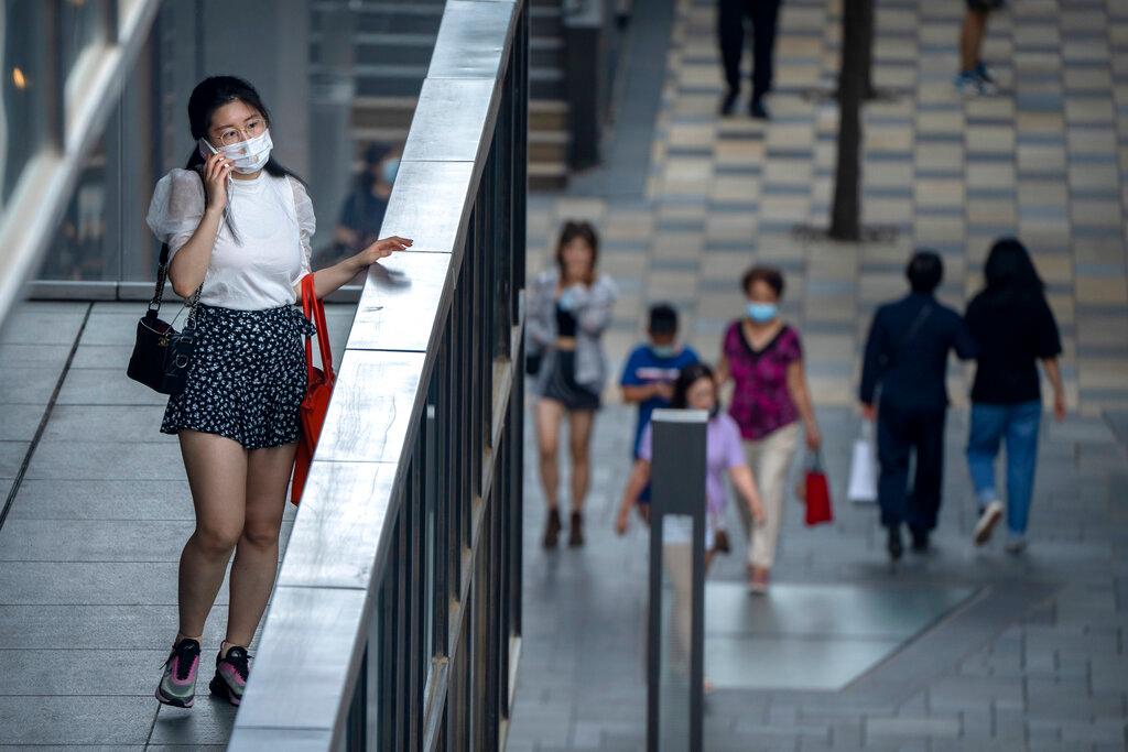 A woman wearing a face mask to prevent the spread of Covid-19 stands on a balcony as she talks on her mobile phone at a shopping mall in Beijing, July 17. Photo: AP