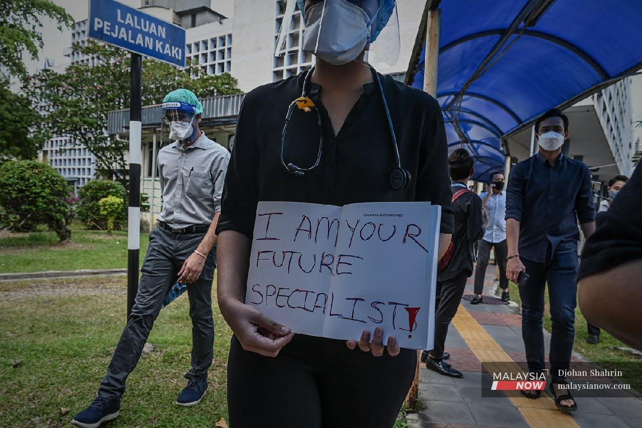 Beberapa orang doktor kontrak berjalan keluar dari lobi utama sambil memegang plakad ketika mengadakan himpunan secara aman di Hospital Kuala Lumpur pada 26 Julai, 2021.