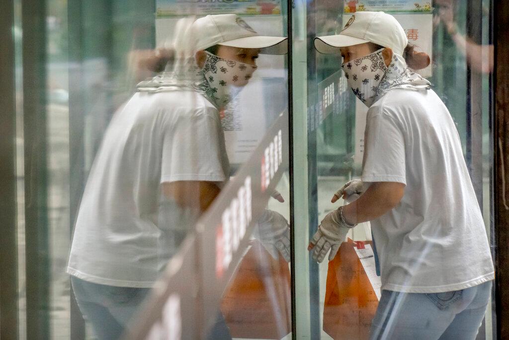 A delivery courier wearing a face mask to protect against Covid-19 is reflected in a window glass as she walks into a restaurant in Beijing, July 27. Photo: AP