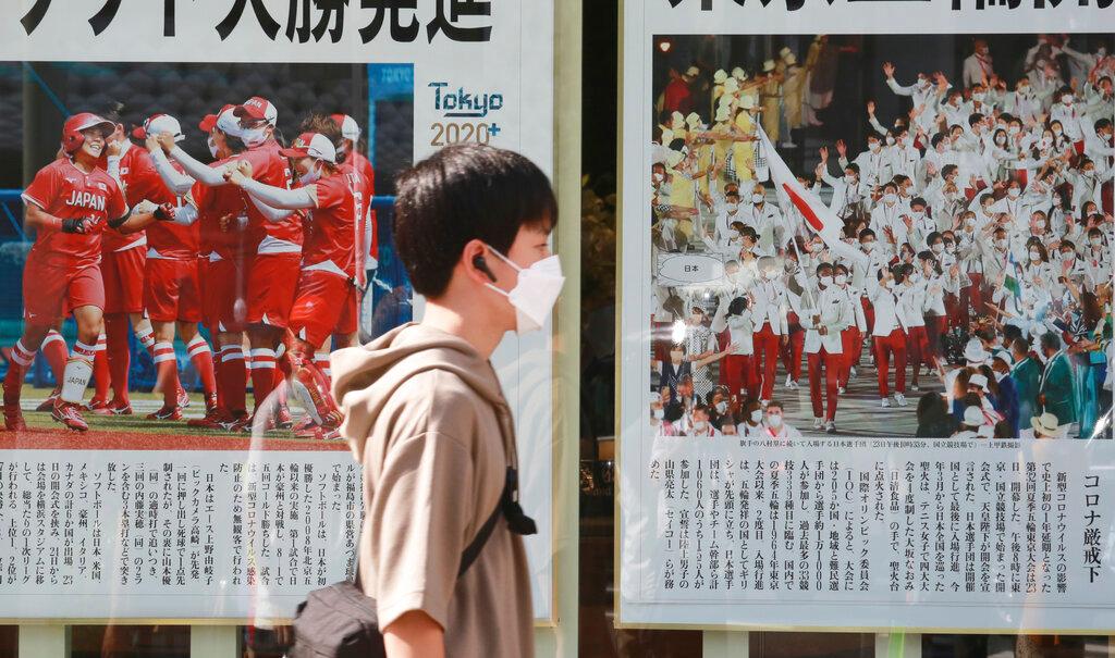 A man wearing a face mask walks past newspapers reporting the start of the Tokyo Olympics in Tokyo, July 24. Photo: AP