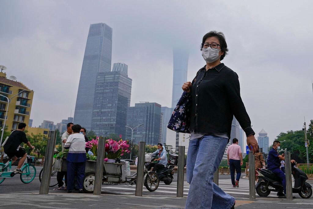 A woman wearing a face mask to help curb the spread of the coronavirus walks by a vendor selling flowers outside a subway station in Beijing, July 22. Photo: AP