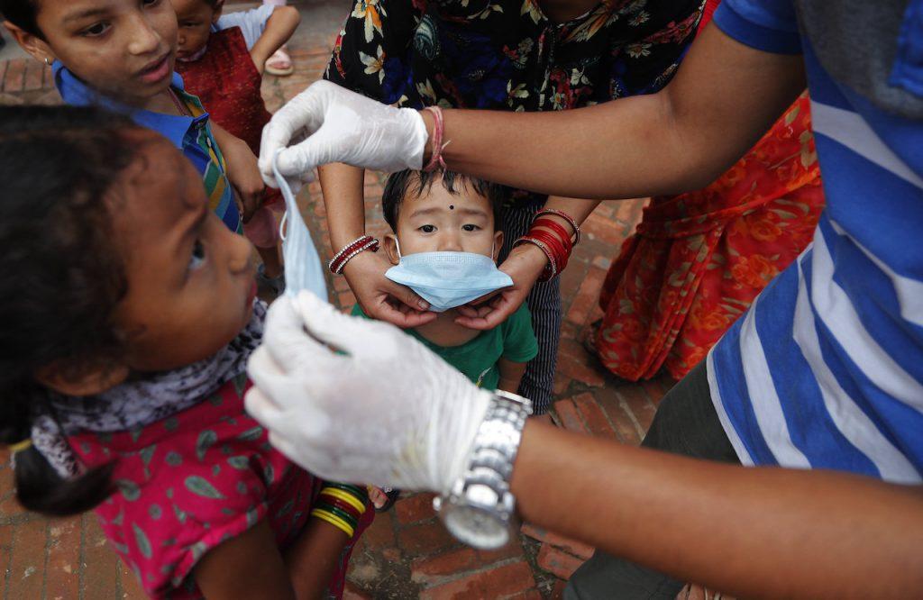 A volunteer hands out free face masks to children to curb the spread of Covid-19 in Lalitpur, Nepal. Photo: AP