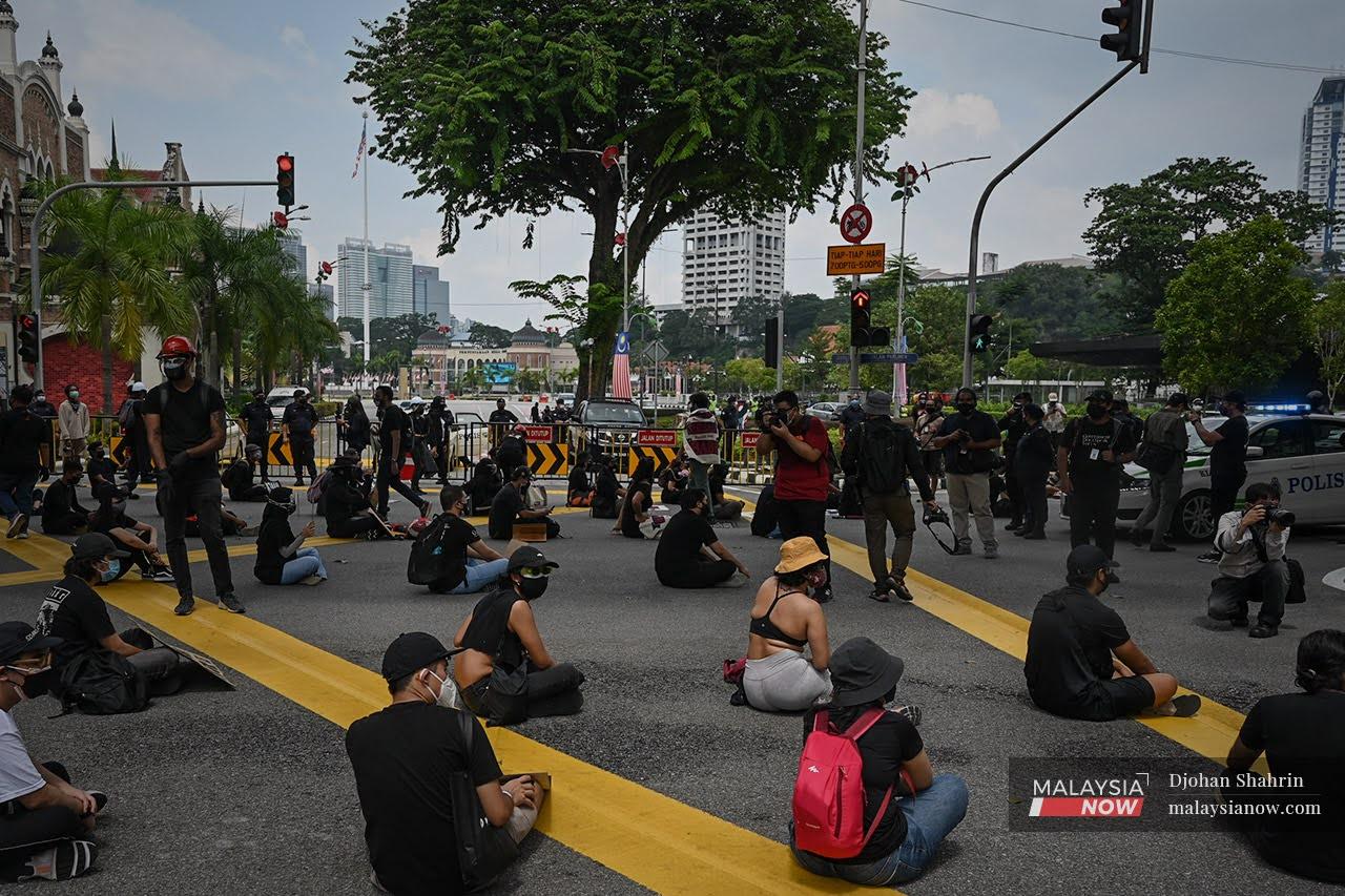 Peserta perhimpunan #Lawan yang memakai baju hitam memegang sepanduk sambil duduk di atas Jalan Tun Perak bagi menyatakan bantahan mereka terhadap kerajaan.