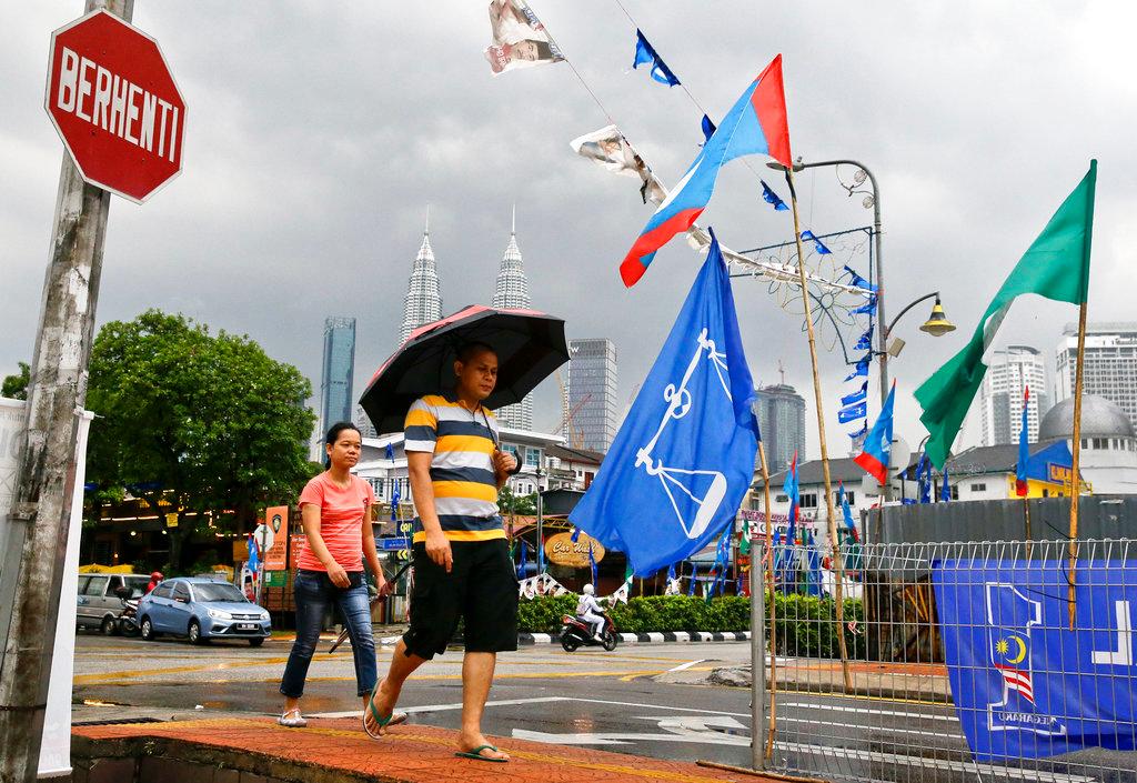 People walk beside flags from different political parties near the Petronas Twin Towers in Kuala Lumpur on May 7, 2018, ahead of the 14th general election which saw Barisan Nasional's fall from federal power. Photo: AP