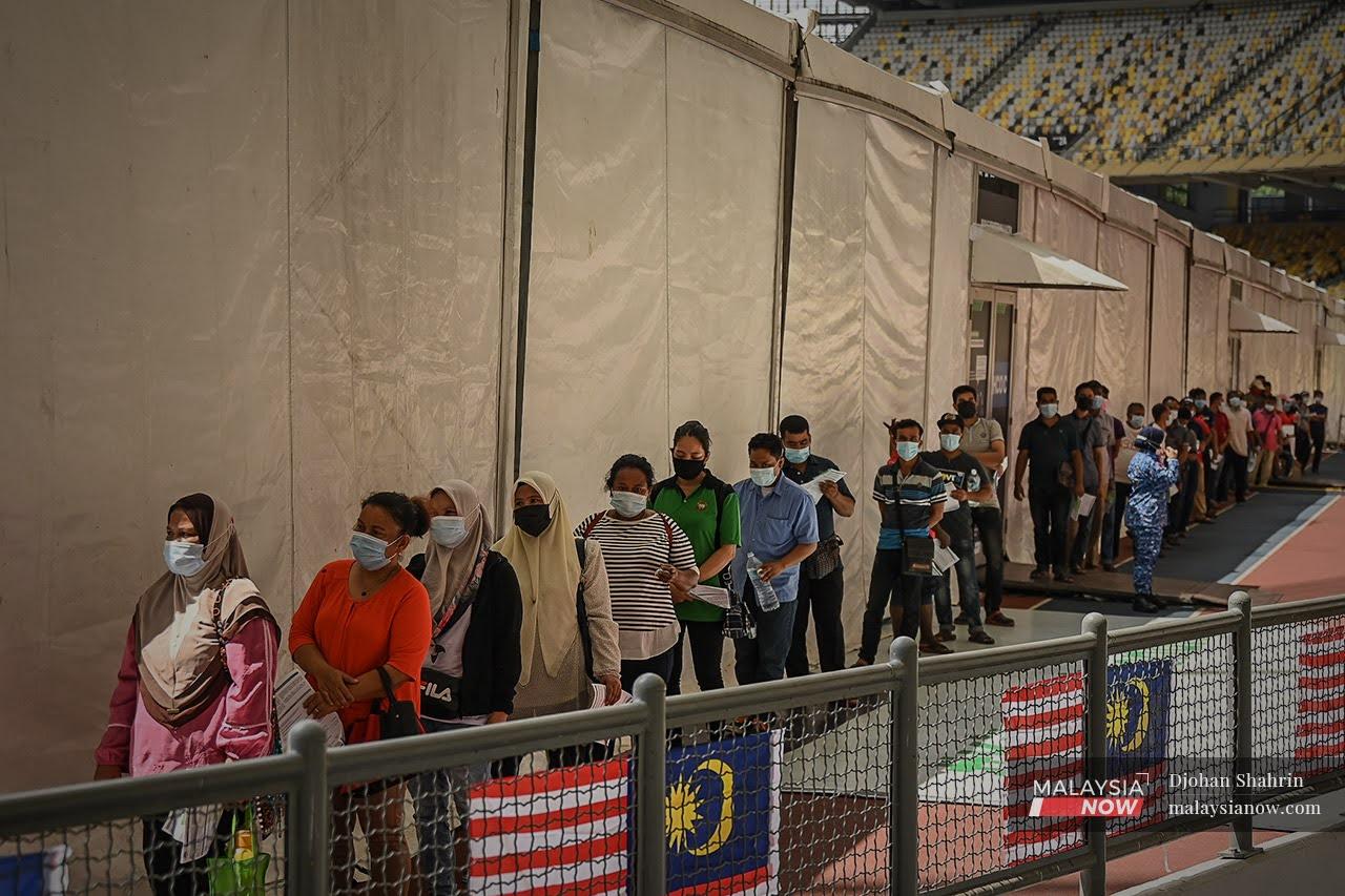 Foreigners who walked in for vaccination wait for their turn to receive a shot of Covid-19 vaccine at Stadium Bukit Jalil in Kuala Lumpur.
