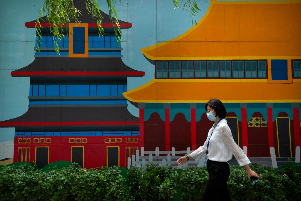 A woman wearing a face mask to protect against the spread of Covid-19 walks past a mural depicting historical landmarks in Beijing, Aug 13. Photo: AP