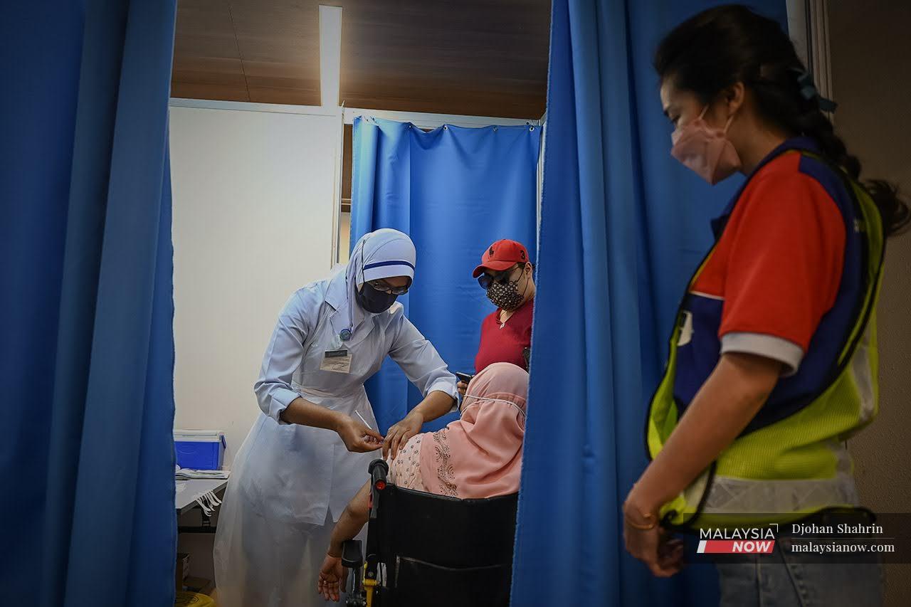 A volunteer from Malaysia Airlines waits while a health worker administers a dose of Covid-19 vaccine to a woman in a wheelchair at the Axiata Arena Bukit Jalil vaccination centre in Kuala Lumpur.