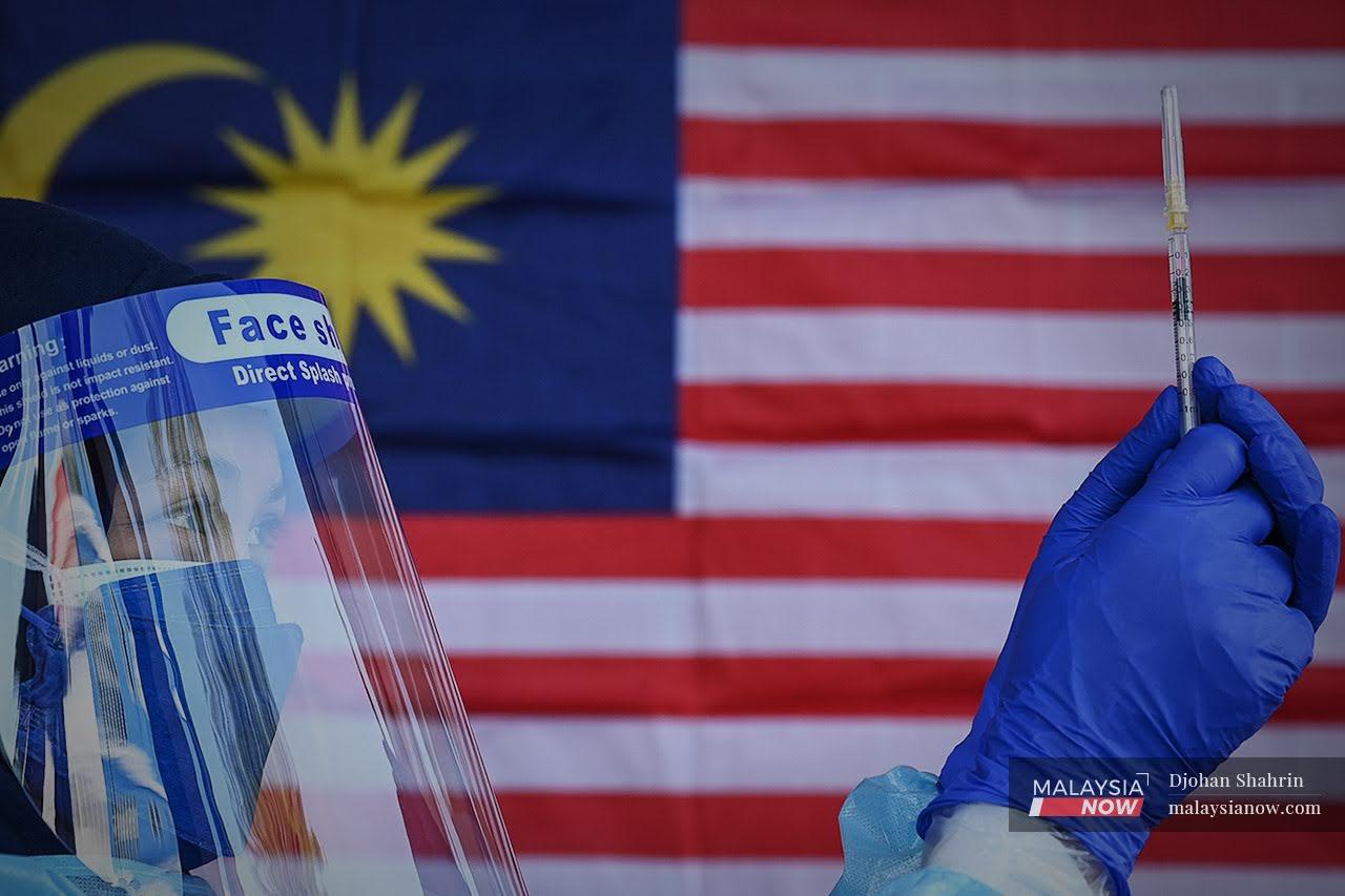 A medical worker prepares a syringe of Covid-19 vaccine against a backdrop of the Malaysian flag at a drive-thru vaccination centre at the Universiti Kebangsaan Malaysia Medical Centre in Cheras.