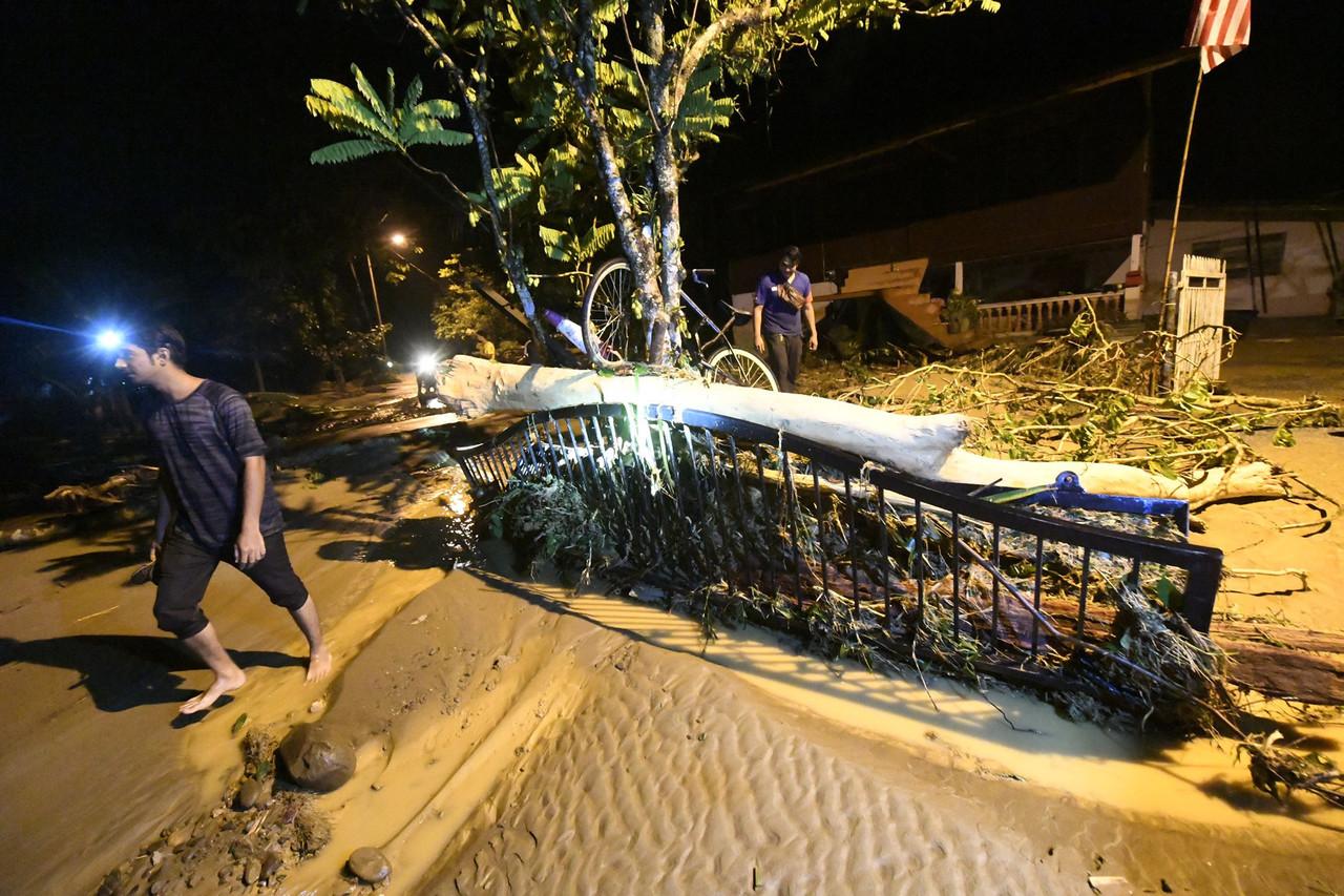 Residents in Yan walk past debris left by the flood which occurred after an upstream rush of water at the waterfall area near Gunung Jerai yesterday. Photo: Bernama