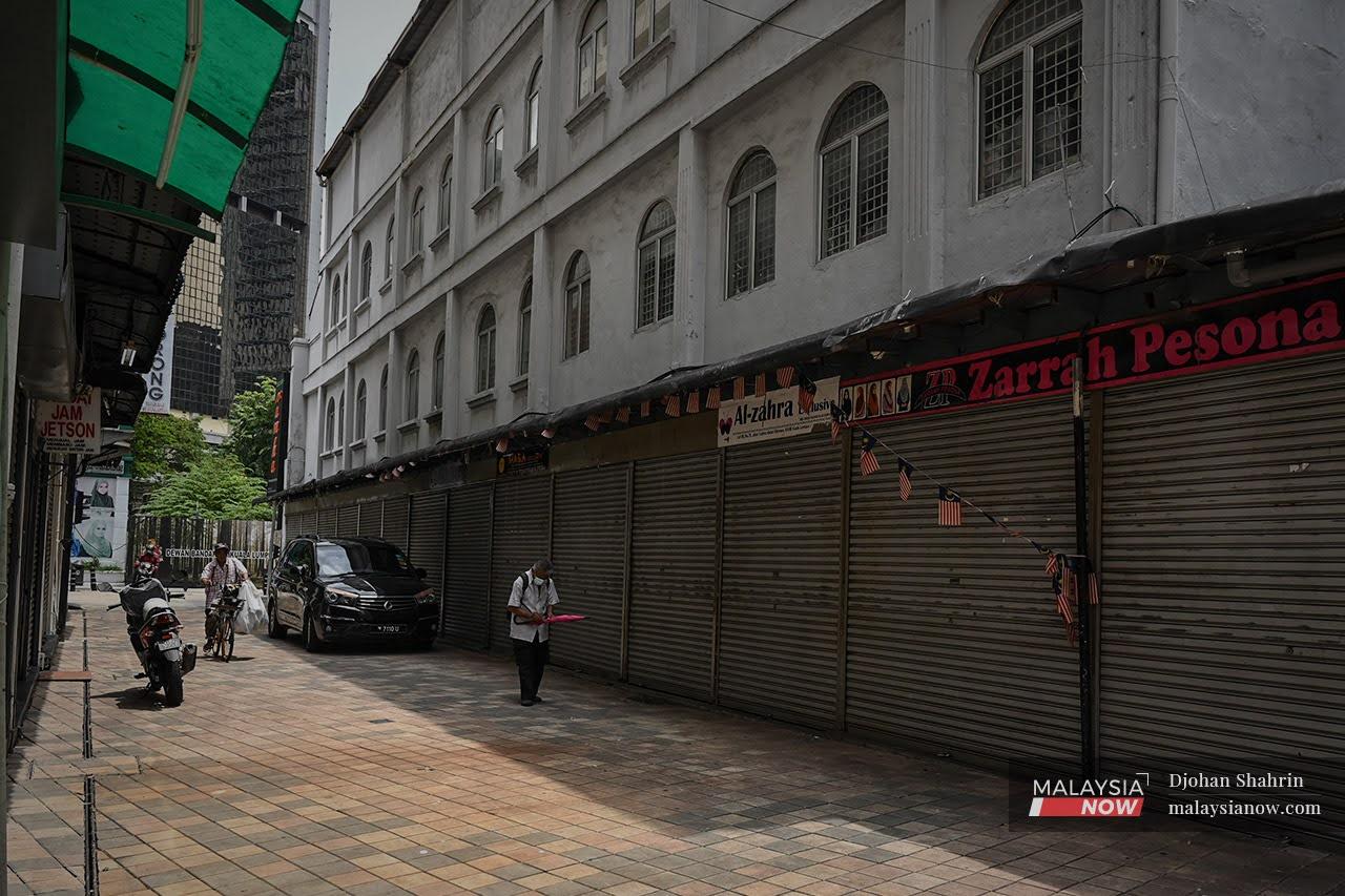Pedestrians walk past a row of shops in Kuala Lumpur which remain closed despite the green light for some businesses to reopen to fully vaccinated customers.