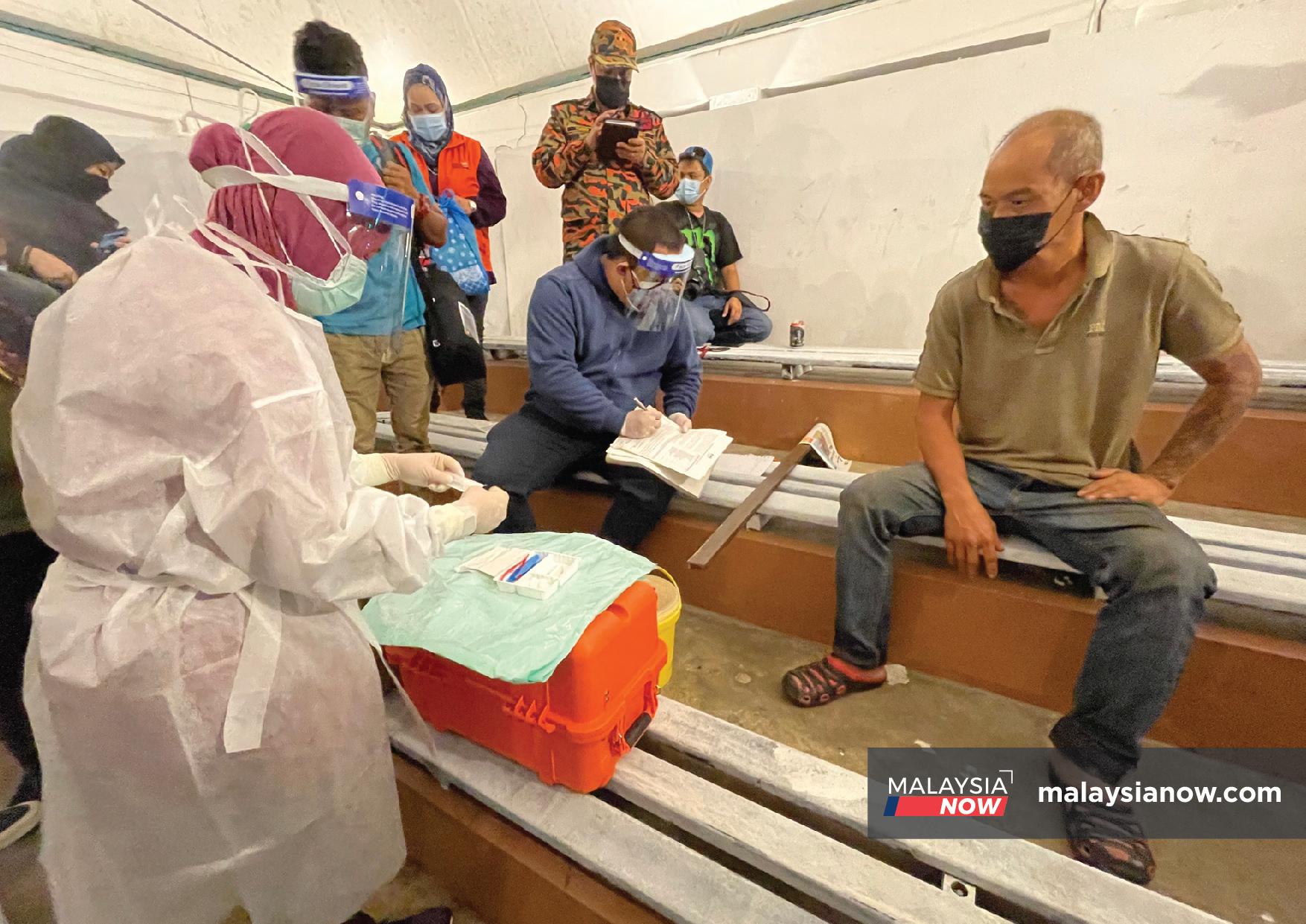 Petugas kesihatan menyiapkan suntikan dan mengambil maklumat gelandangan yang bakal menerima vaksin di Kuching.