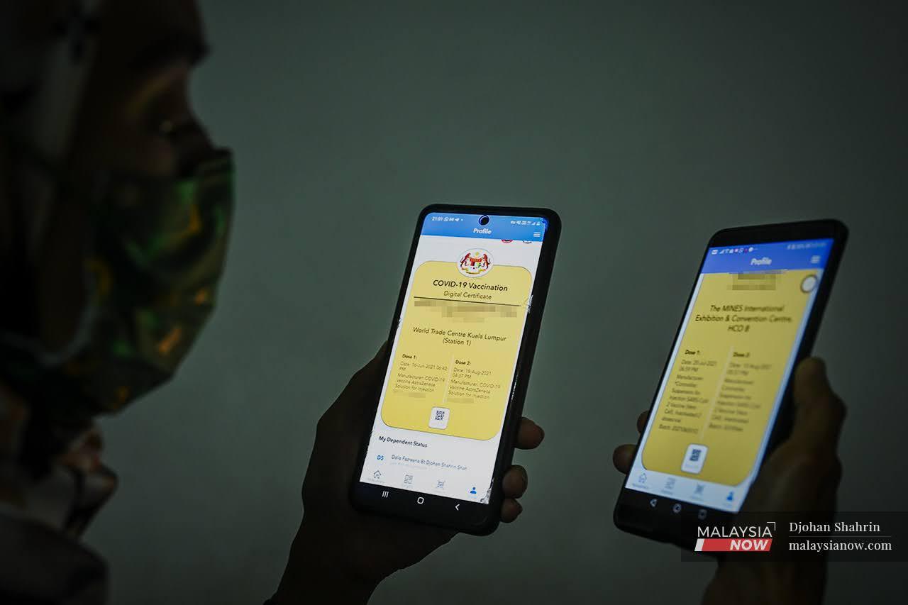 Seorang wanita melihat perbandingan dua sijil digital vaksinasi di dalam aplikasi Mysejahtera pada dua telefon bimbit. Sijil vaksinasi membolehkan penerima vaksin lengkap menikmati kelonggaran SOP kesihatan Covid-19.
