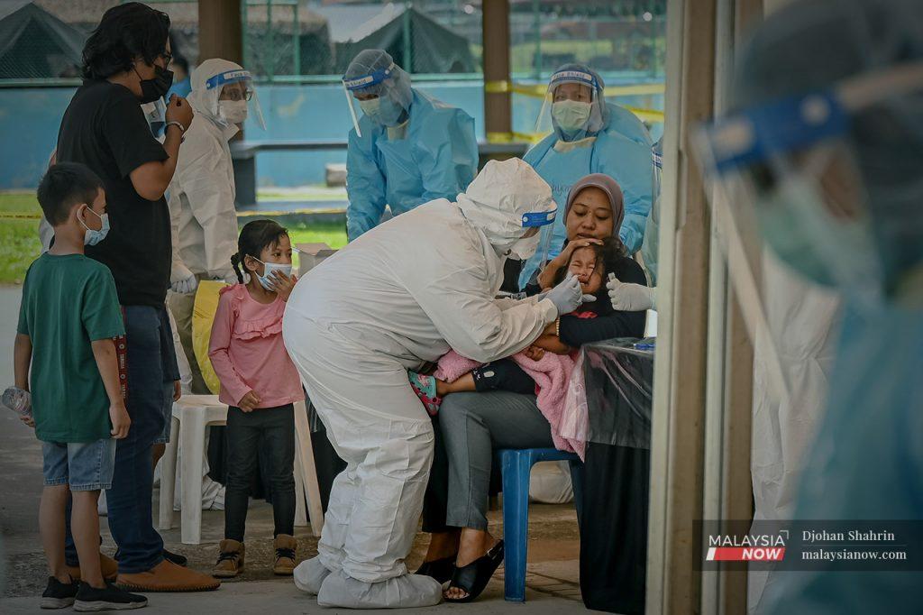 Seorang kanak-kanak menangis ketika petugas kesihatan mengambil sampel ujian swab Covid-19. 30% dari keseluruhan kes positif di Sarawak terdiri daripada kanak-kanak yang tidak layak menerima vaksin ketika ini.