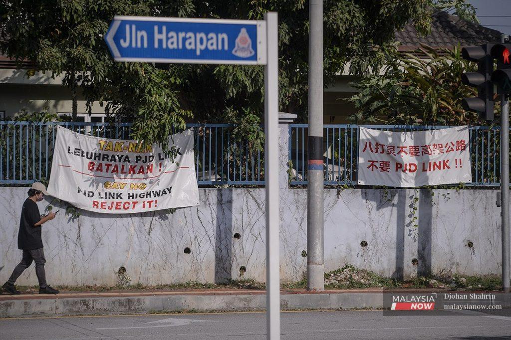 A man walks past banners in multiple languages objecting to the PJD Link along Jalan Harapan in Petaling Jaya. Residents have been up in arms over the highway project which will cut through various parts of the district.