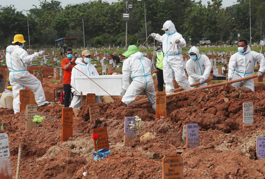 Workers in protective gear lower the coffin of a Covid-19 victim for burial at the special section of the Pedurenan cemetery designated to accommodate the surge in deaths during the coronavirus outbreak in Bekasi, West Java, Indonesia, Aug 12. Photo: AP