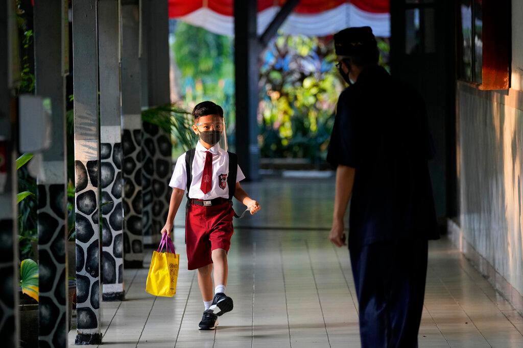 A staff member greets a student during the first day of school reopening at an elementary school in Jakarta, Indonesia, Aug 30. Photo: AP