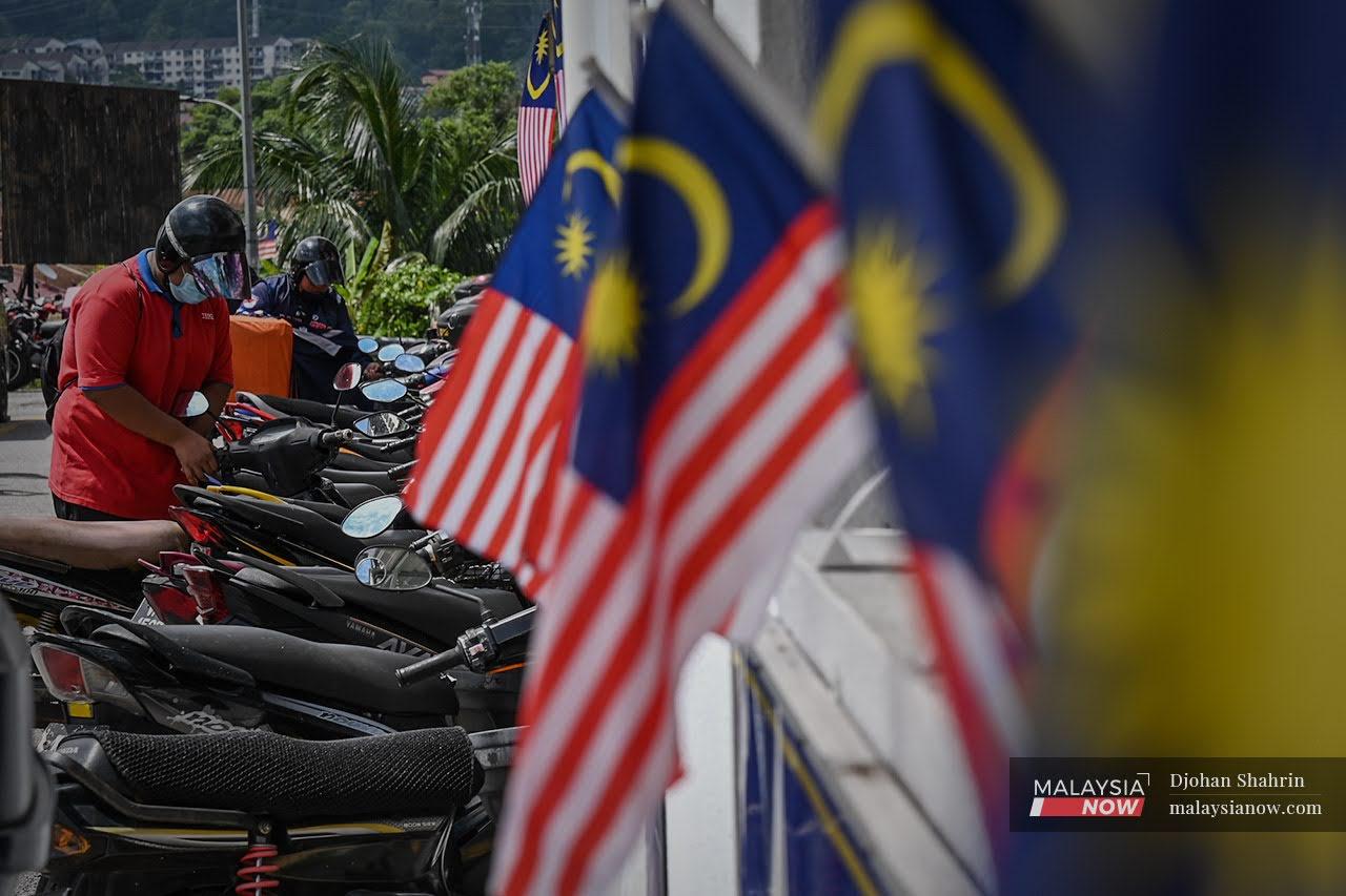 A motorcyclist wearing a face mask checks his bike at the car park area of the Taman Industri Lembah Jaya flats in Ampang, Selangor, which has been decorated with Malaysian flags in honour of Merdeka Day.