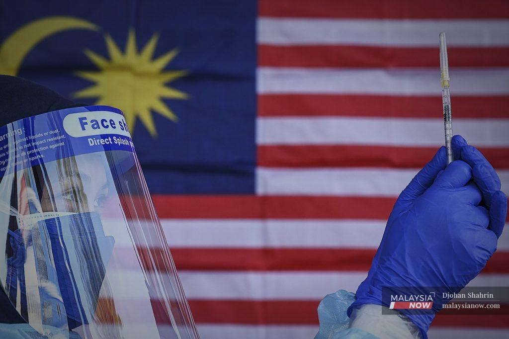 A health worker holds up a syringe of Covid-19 vaccine against a Jalur Gemilang backdrop. The Klang Valley has so far vaccinated nearly 90% of its adult population.