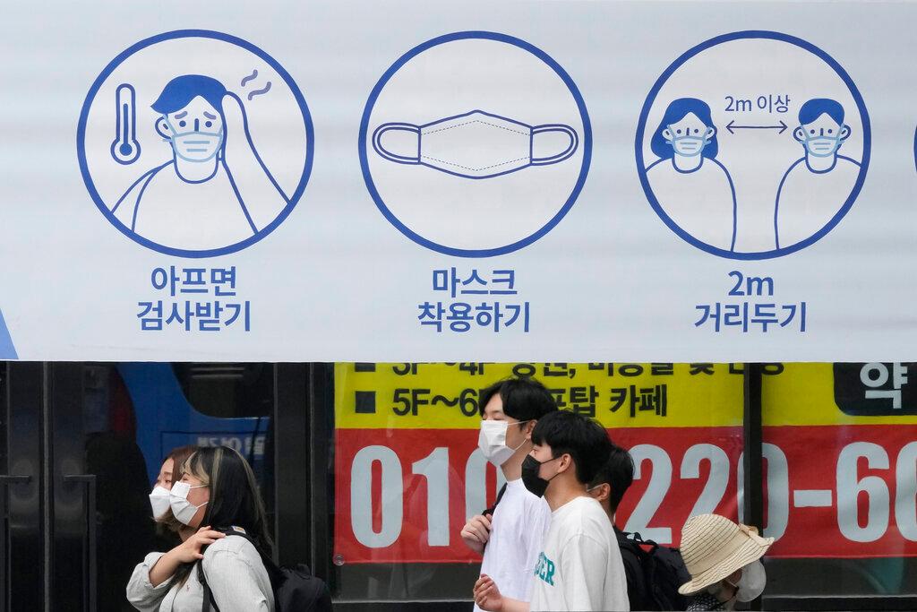 People wearing face masks pass by a banner displaying precautions against the coronavirus on a street in Seoul, South Korea, Aug 20. Photo: AP