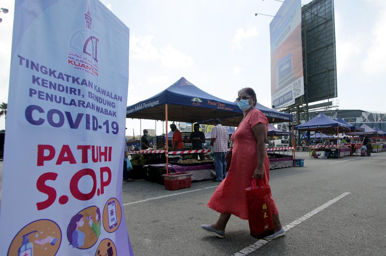 A woman carries a shopping bag past a banner reminding customers to follow health SOPs at a farmers market in Kuantan, Pahang. Photo: Bernama
